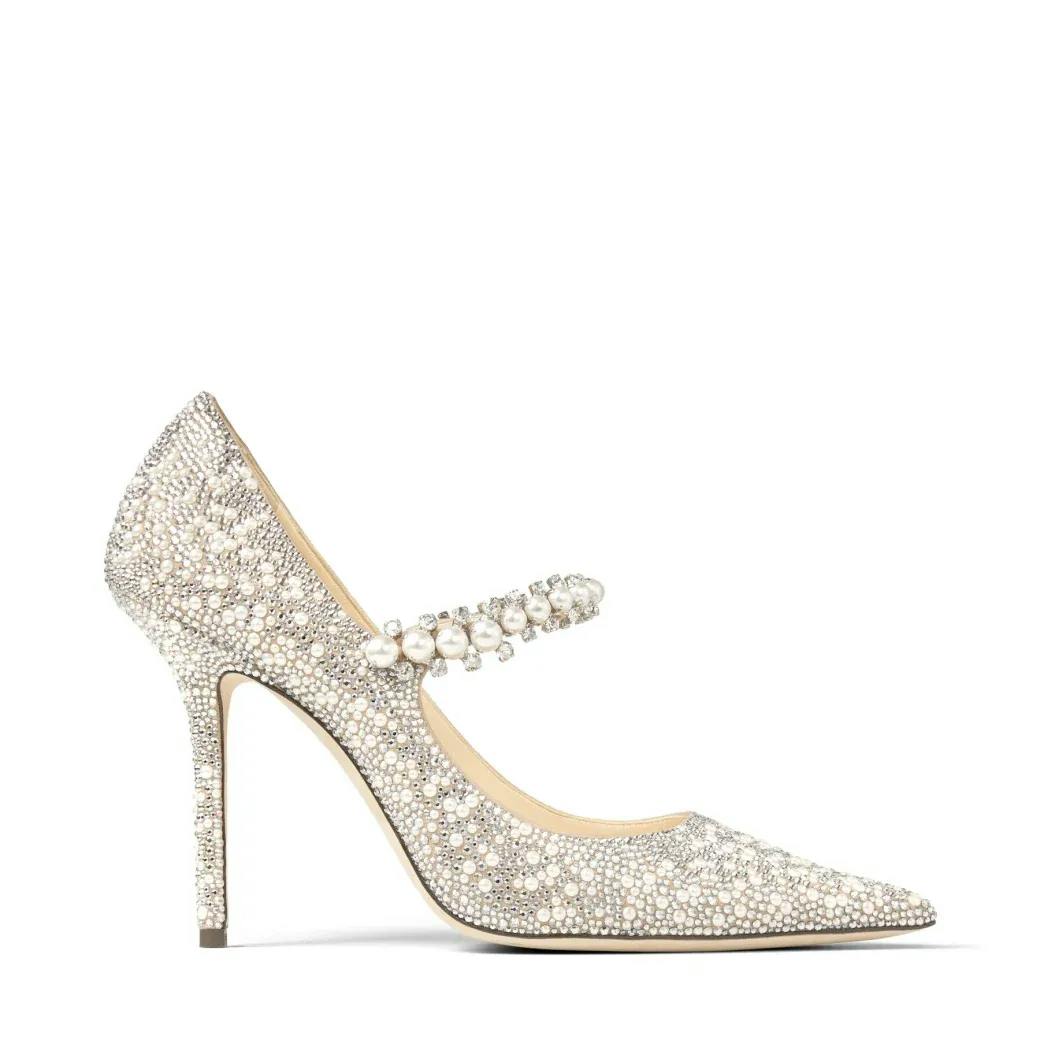 A sparkling high-heeled shoe covered in rhinestones. It has a pointed toe and a Mary Jane strap adorned with pearl accents. The shoe features a stiletto heel and a luxurious, elegant design.