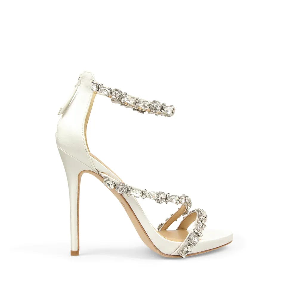 Side view of an elegant, high-heeled sandal with white straps adorned with sparkling, silver-tone rhinestones. The shoe features a closed back and a zipper for closure. The stiletto heel and open toe design add to its sophisticated appearance.