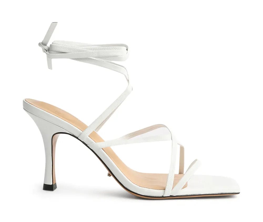 A white high-heeled sandal with multiple thin straps that crisscross over the foot and wrap around the ankle. The shoe features a pointed heel and a square open toe design, with a minimalist and elegant aesthetic.
