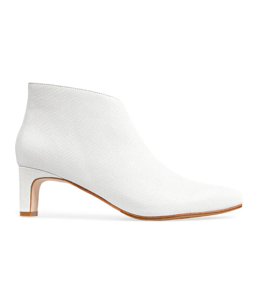 A stylish white ankle boot with a short block heel and a side zipper. The shoe has a sleek and modern design with a smooth finish, and the sole is a light brown color.