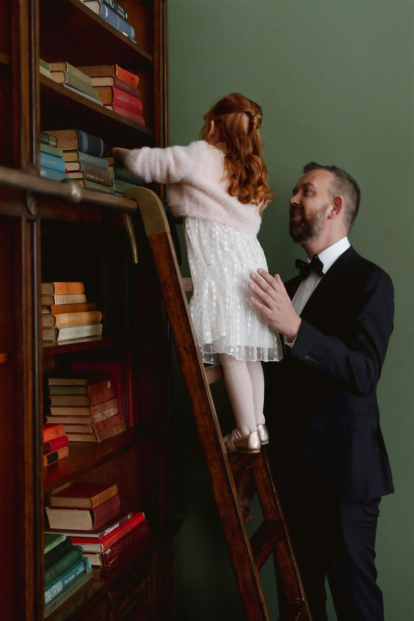 Father helping daughter on book case ladder