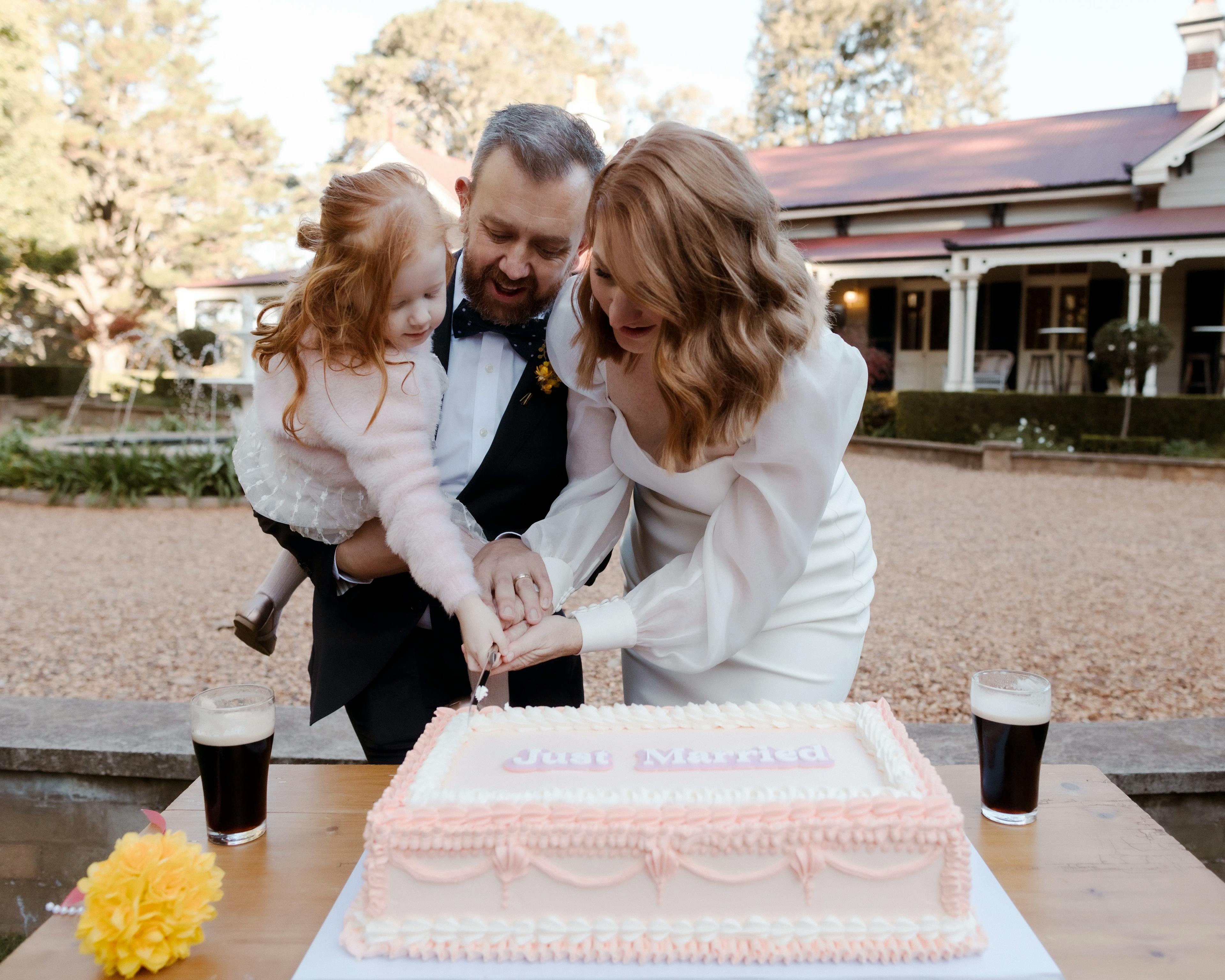 Bride, groom and daughter cutting cake