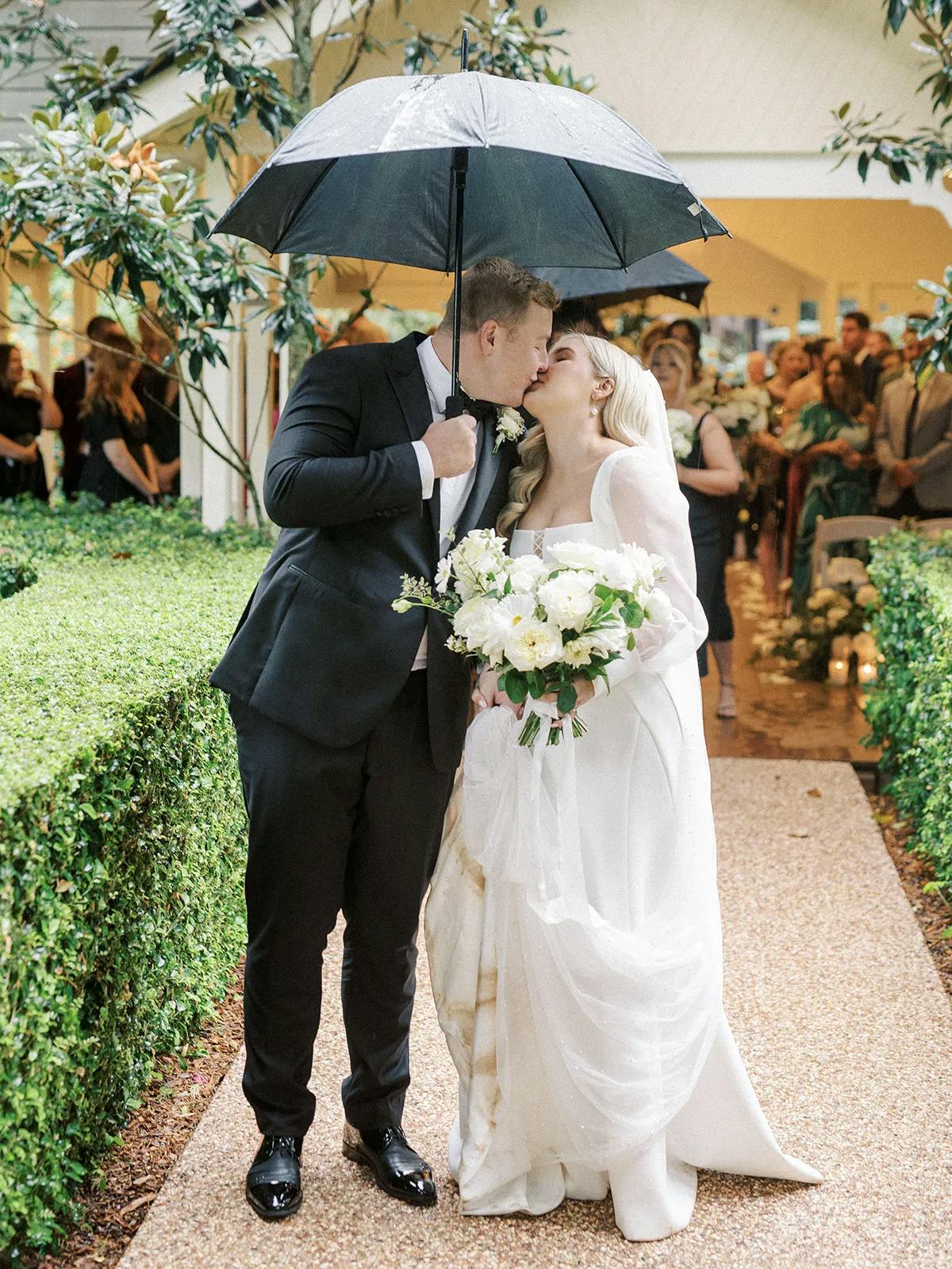 Bride and groom kissing under umbrella