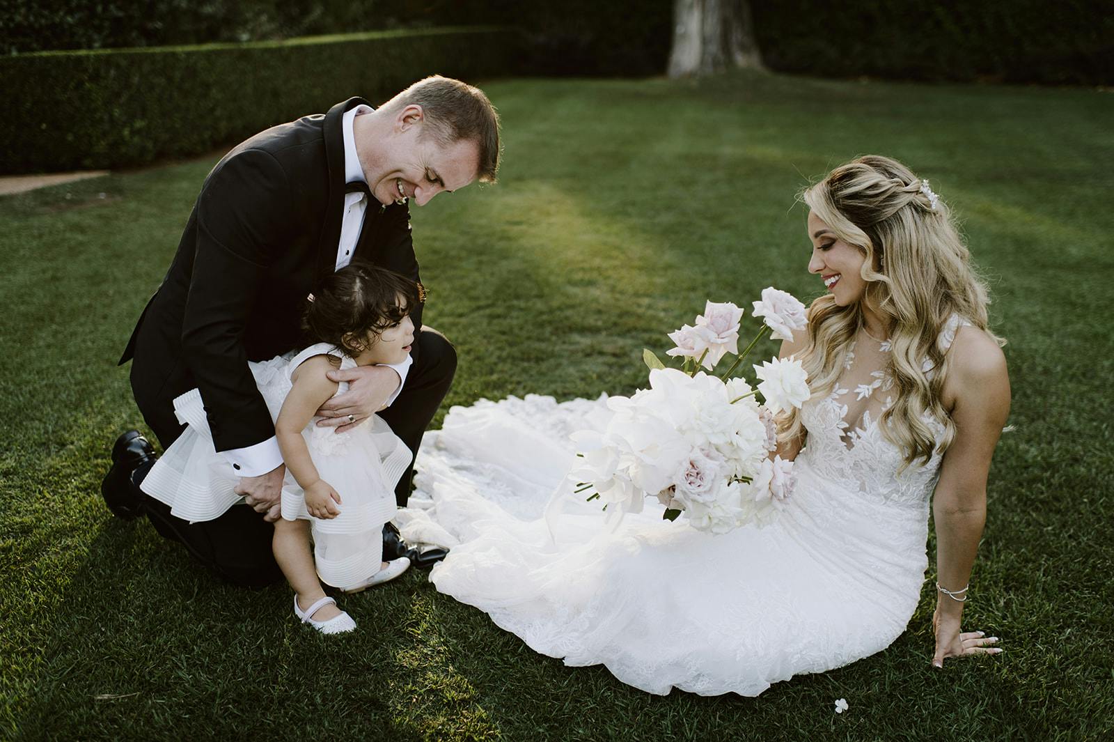 Bride, groom and daughter sitting on grass