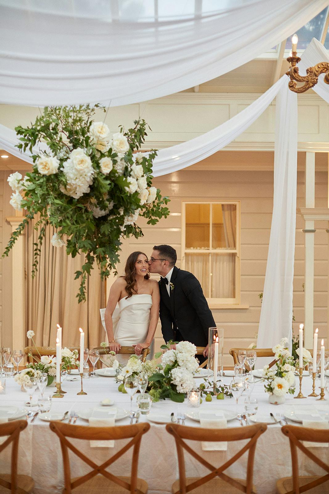 Bride and groom kissing in room with hanging flowers