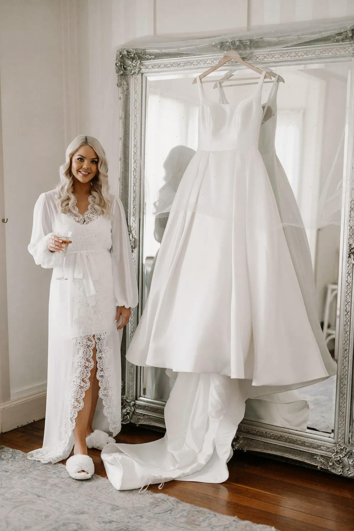 Bride standing next to wedding dress hanging on mirror