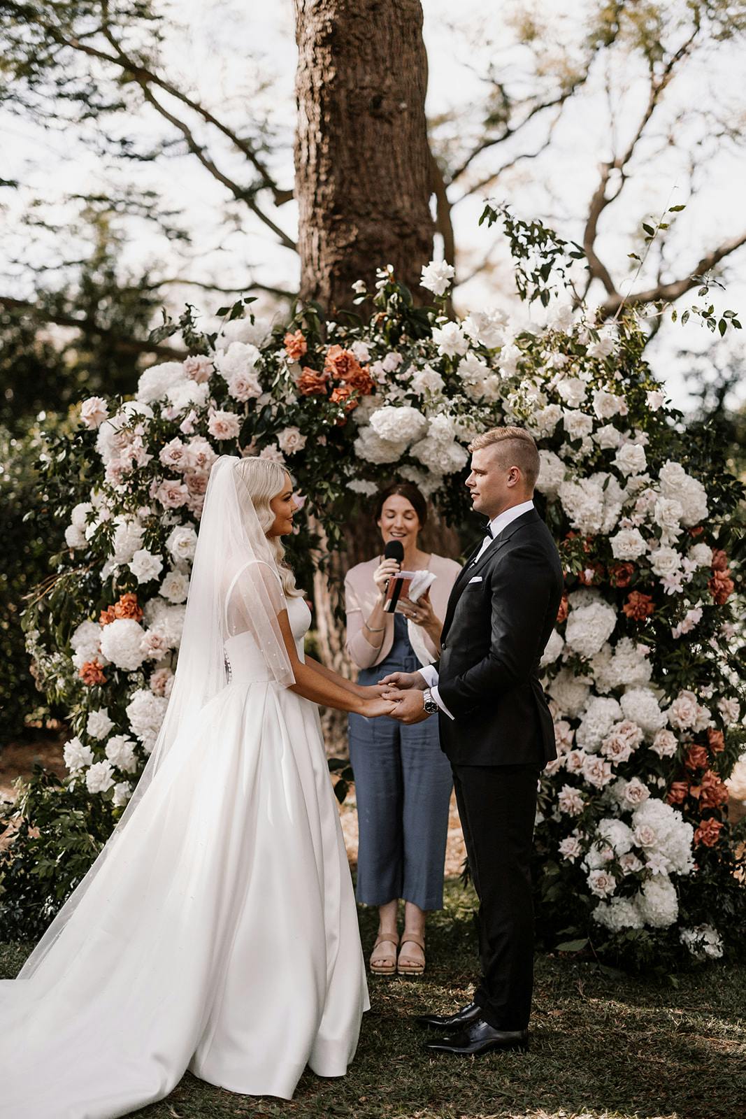Bride and groom standing in front of floral arbour