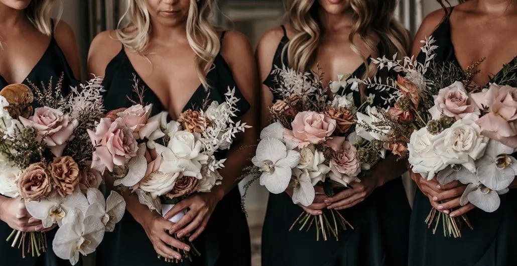 Four women in dark dresses hold bouquets of flowers, including white orchids, pink roses, and dried foliage. The image focuses on the floral arrangements and the upper bodies of the individuals, with a blurred background.