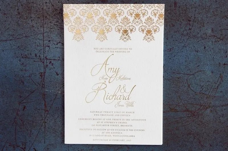 A wedding invitation with an ornate gold floral design at the top. The text reads: "You are cordially invited to celebrate the wedding of Amy Marie Henderson and Richard James Willis. Saturday, March 21, 2015, at St Stephen’s Chapel, Brisbane. Reception to follow.