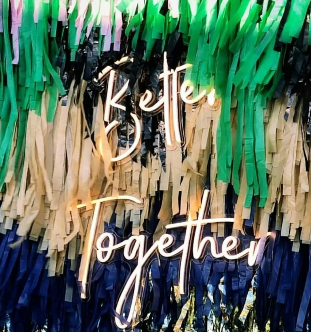 A festive fringe backdrop featuring green, pink, beige, and blue tassels with a neon sign in front that reads "Better Together" in cursive letters.