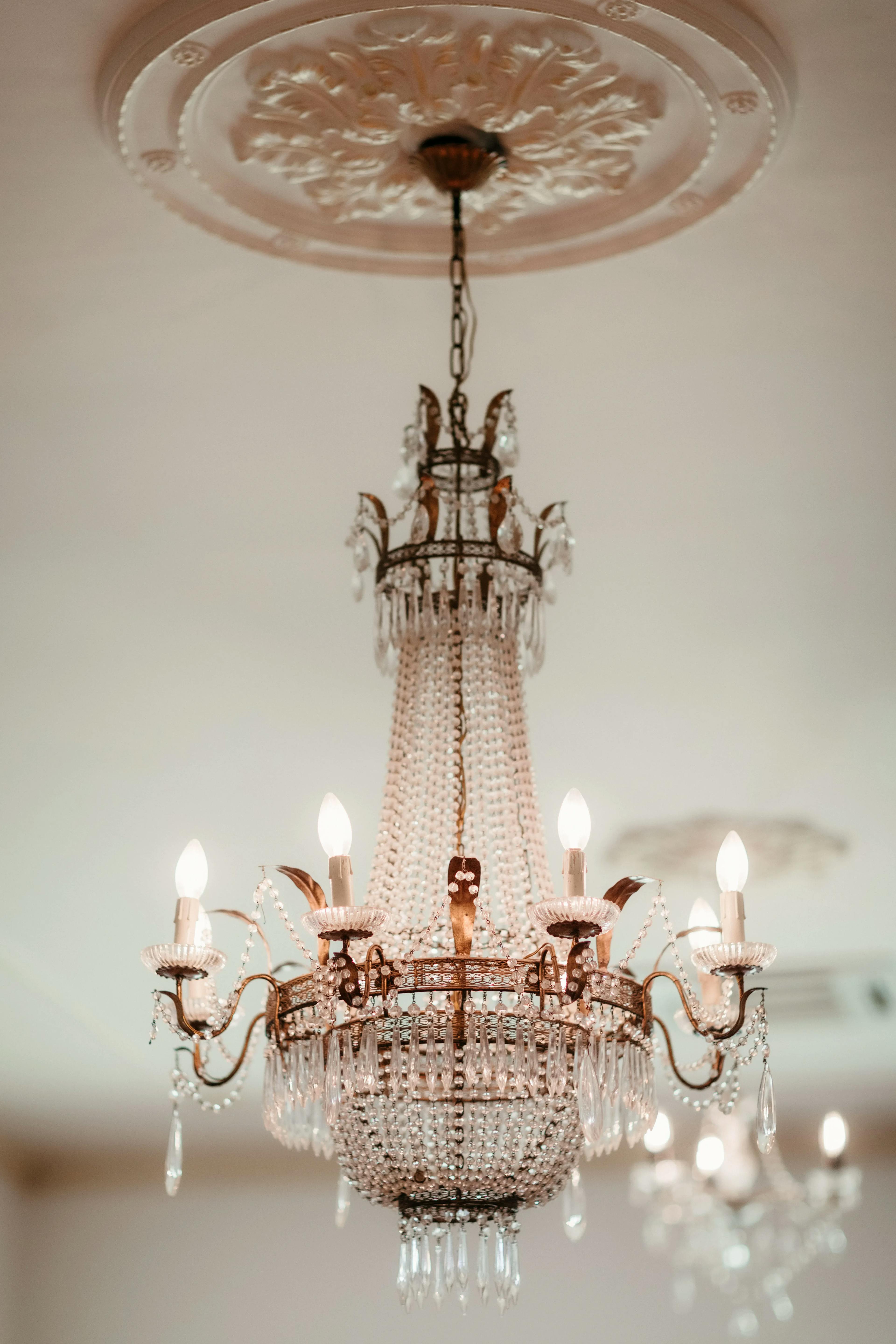 An elegant chandelier with multiple lit candle-like bulbs and hanging crystal ornaments is suspended from an ornate ceiling medallion in a well-lit room.