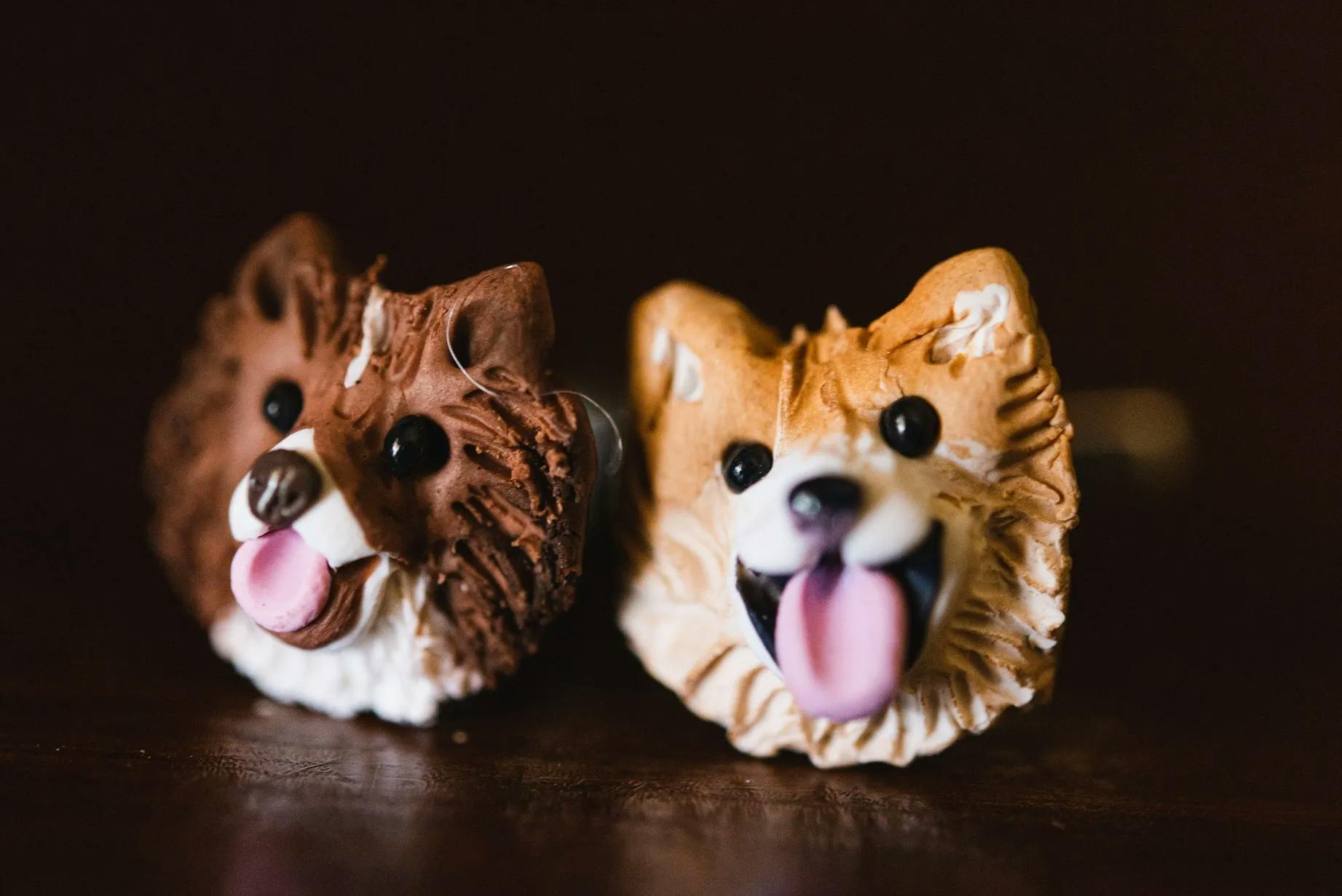Two detailed dog face cufflinks sit side by side. The left one features a fluffy brown dog with a pink tongue out, while the right one resembles a tan and white dog with a wide smile and tongue out. Both have black button eyes, capturing a playful expression.
