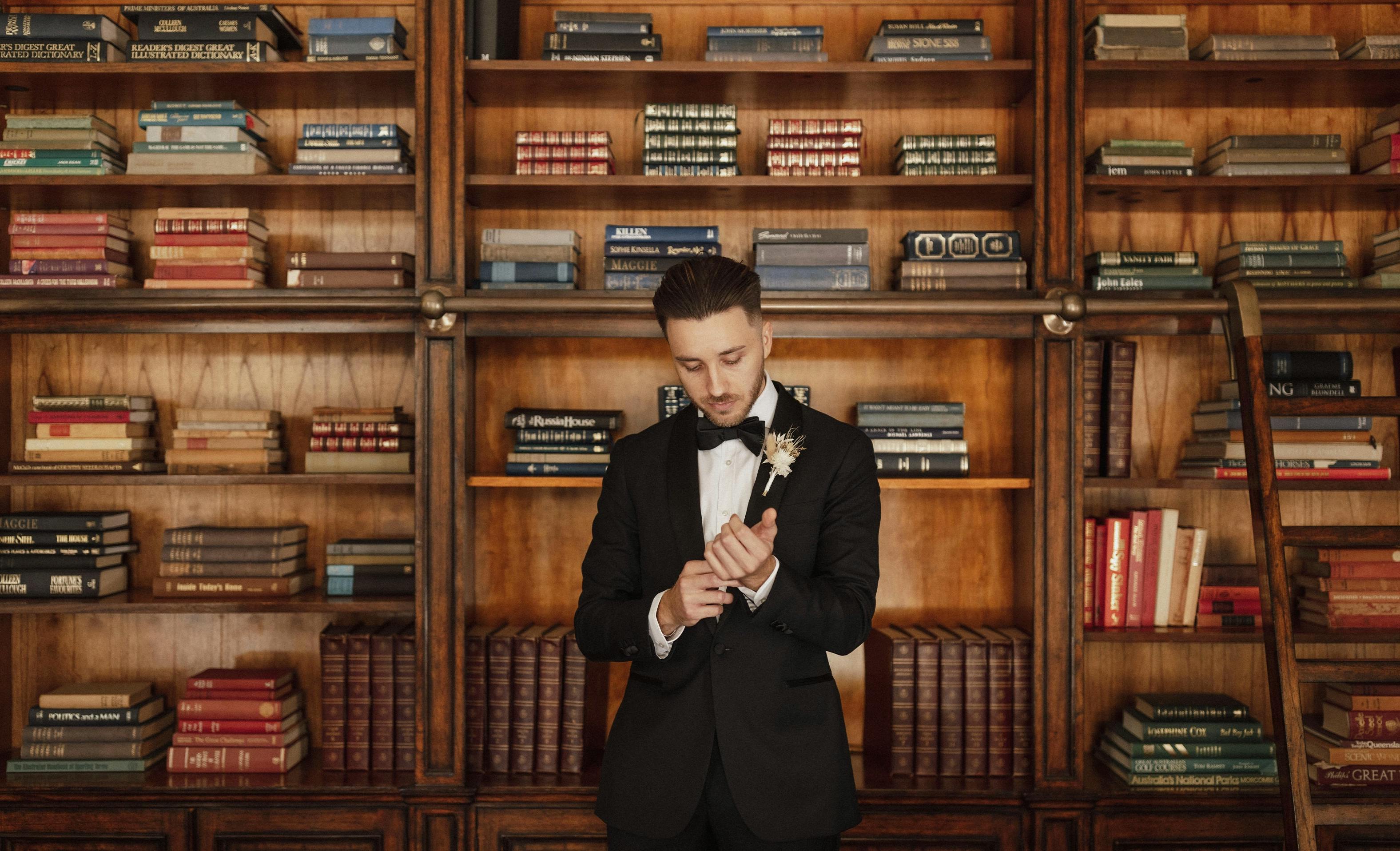 Groom stands in front of library bookcase