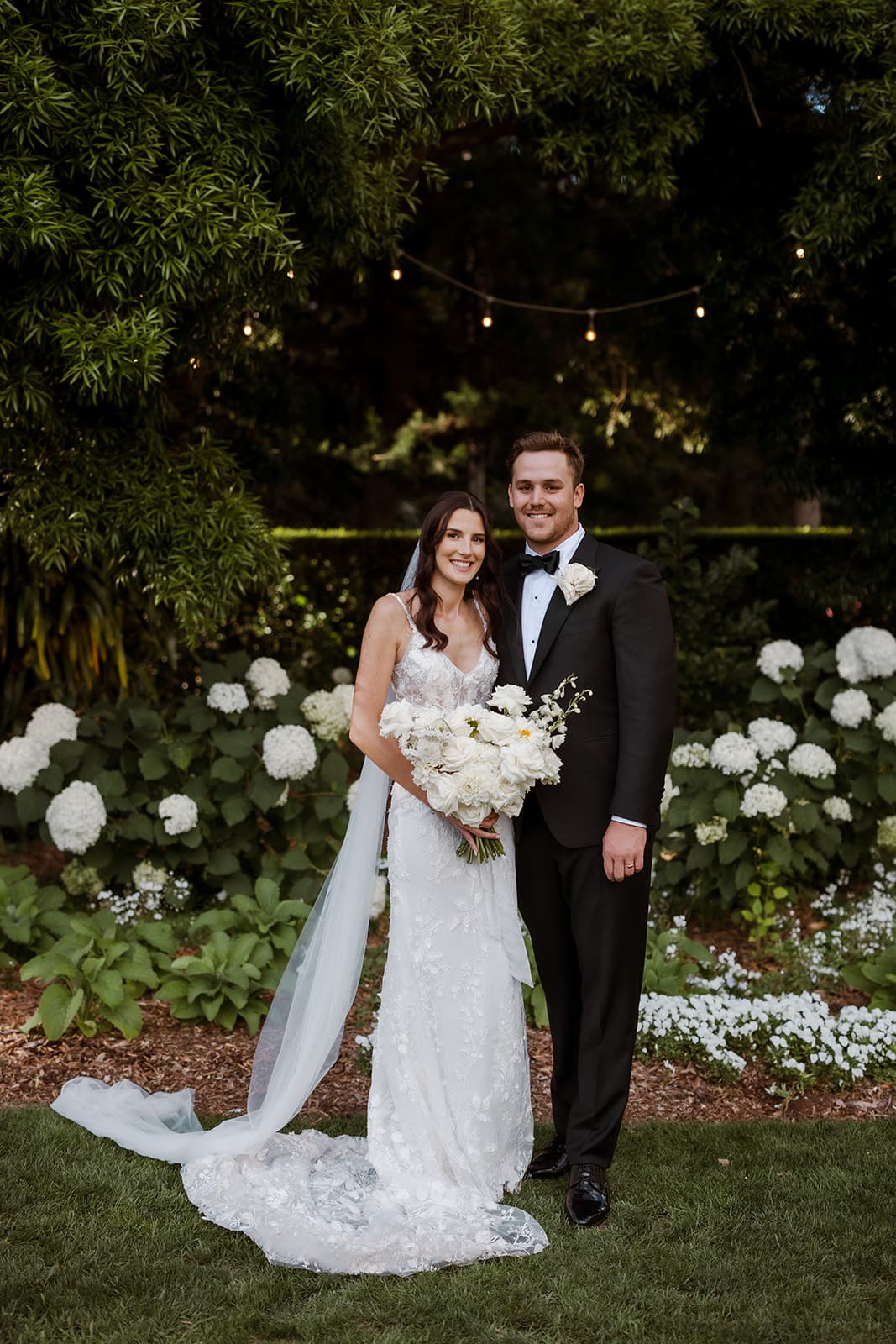 Bride and groom standing in front of white flowers