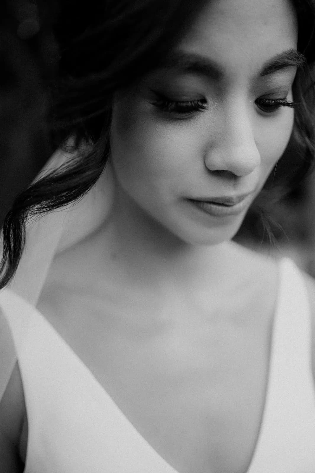 A black-and-white close-up of a young woman with her eyes closed, wearing a bridal dress and veil. Her hair is styled in soft waves, and she appears serene and contemplative. Only her face, neck, and shoulders are visible.