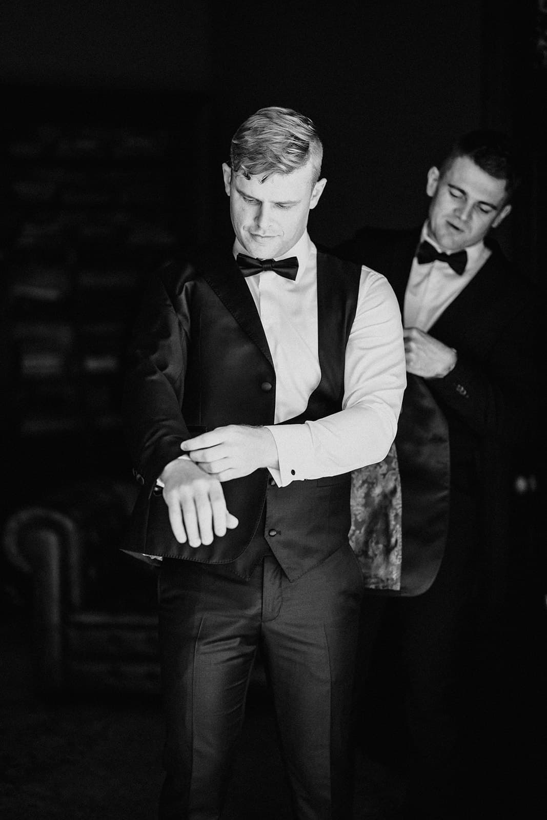 Groomsman assisting groom with suit jacket