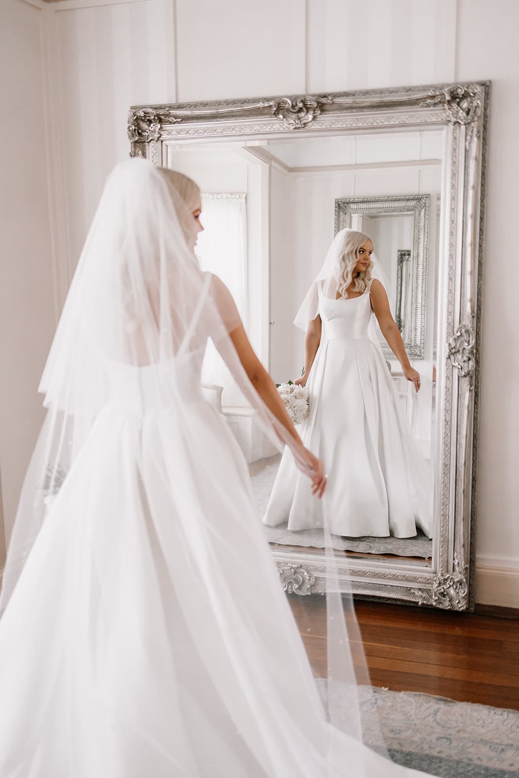 Bride putting on veil in front of mirror