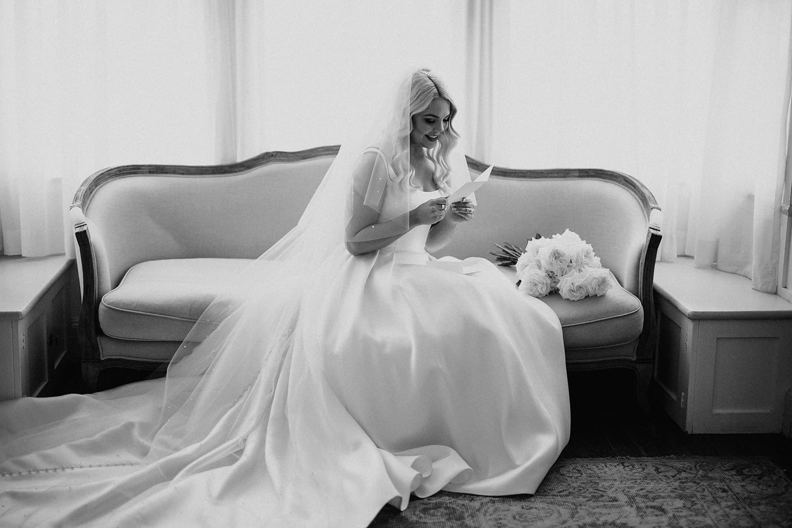 Bride sitting on chaise reading card