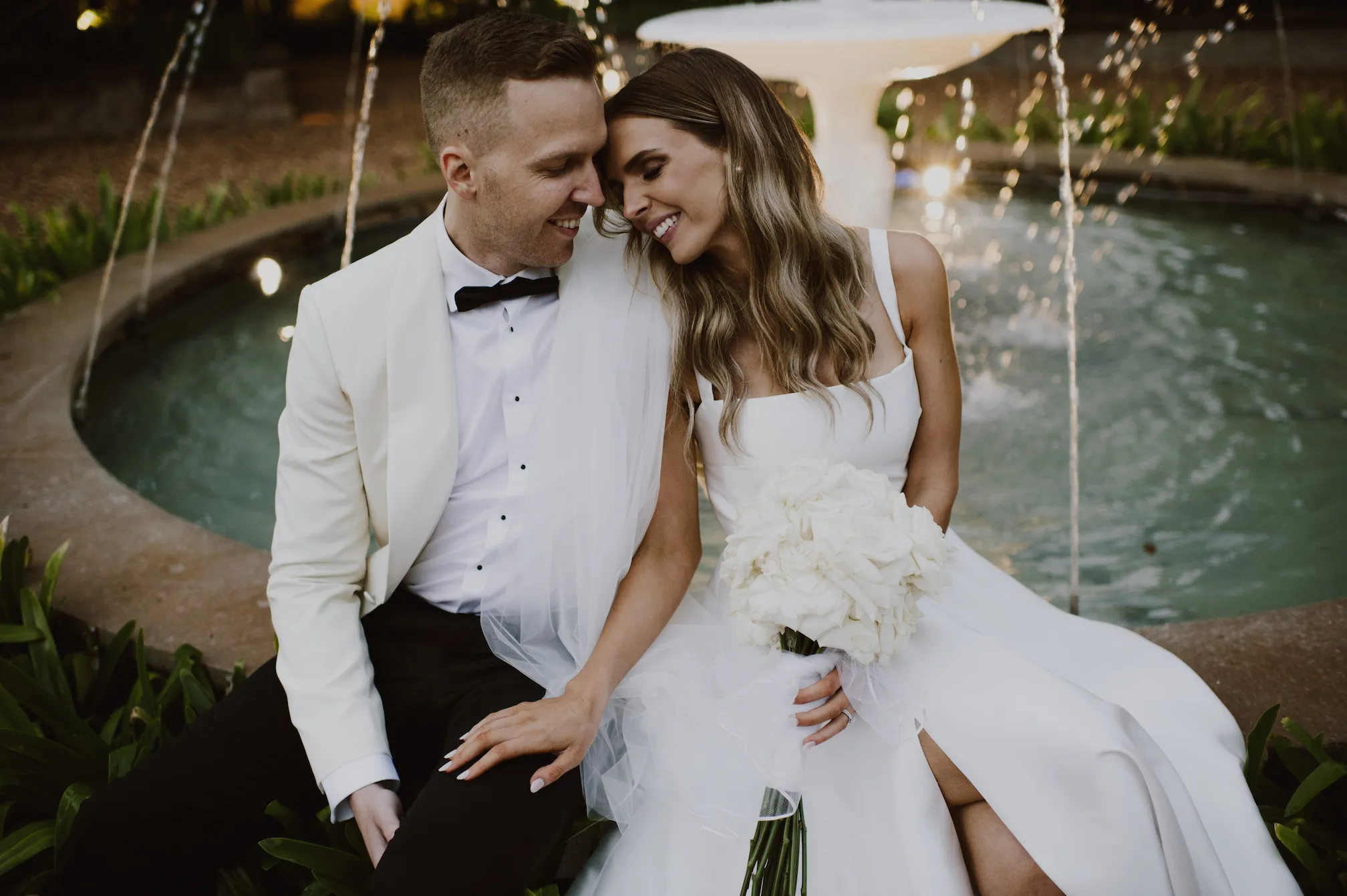 Bride and groom sitting next to fountain