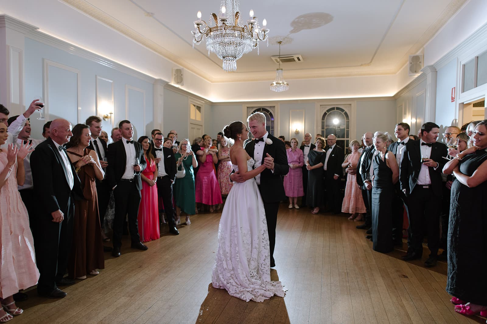 a newly married couple enjoy a first dance together surrounded by their friends and family