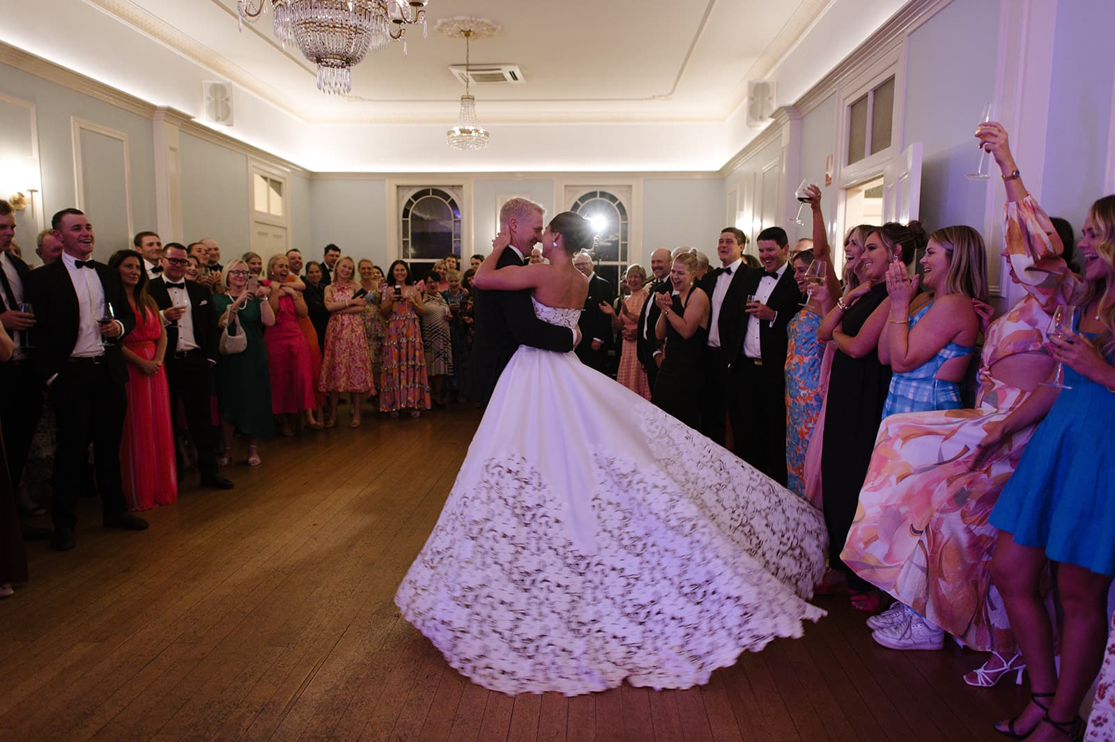 a newly married couple enjoy a first dance together surrounded by their friends and family