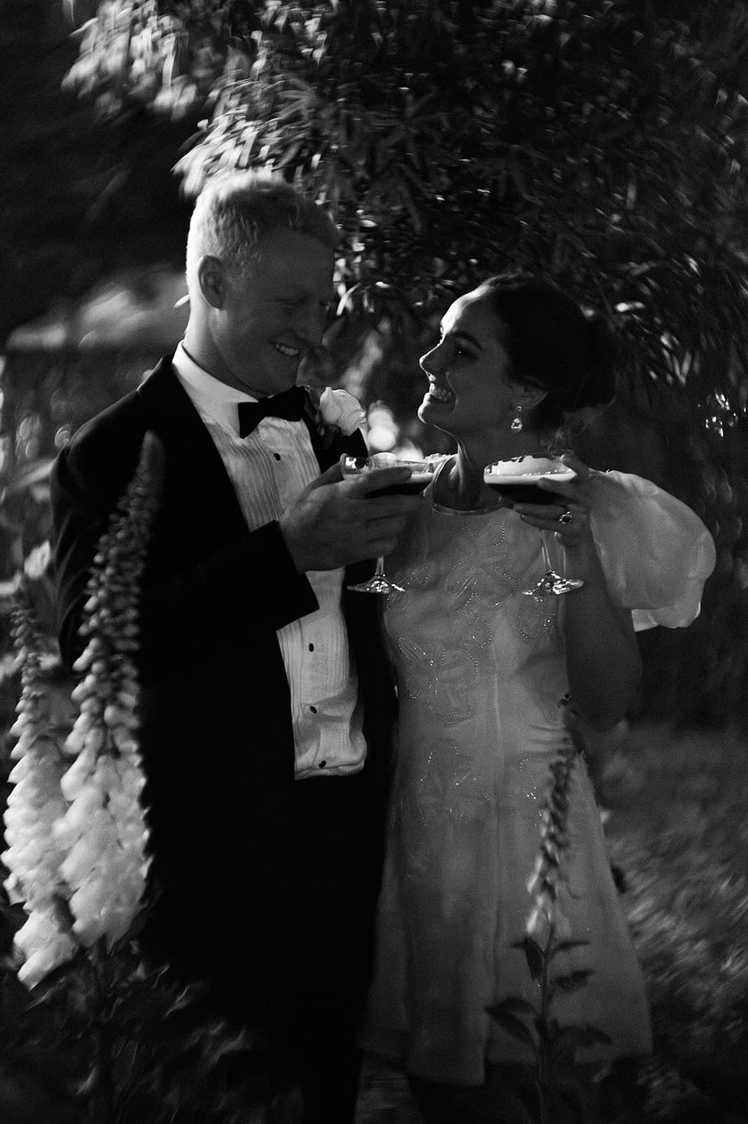 a newly married couple walking through the grounds of gabbinbar at night holding drinks